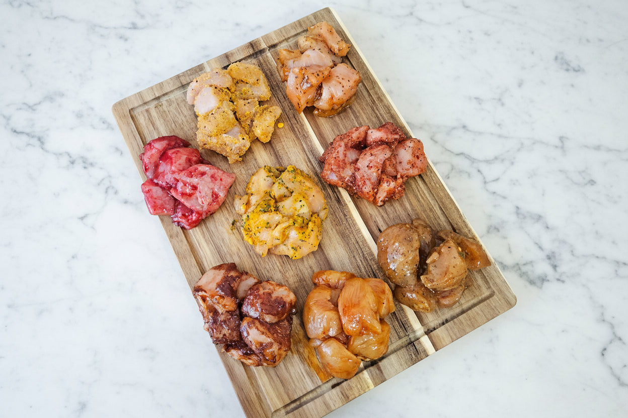 A variety of seasoned and marinated diced chicken pieces on a wooden board, representing the different flavors included in the Gourmet Diced Chicken Taster Selection.