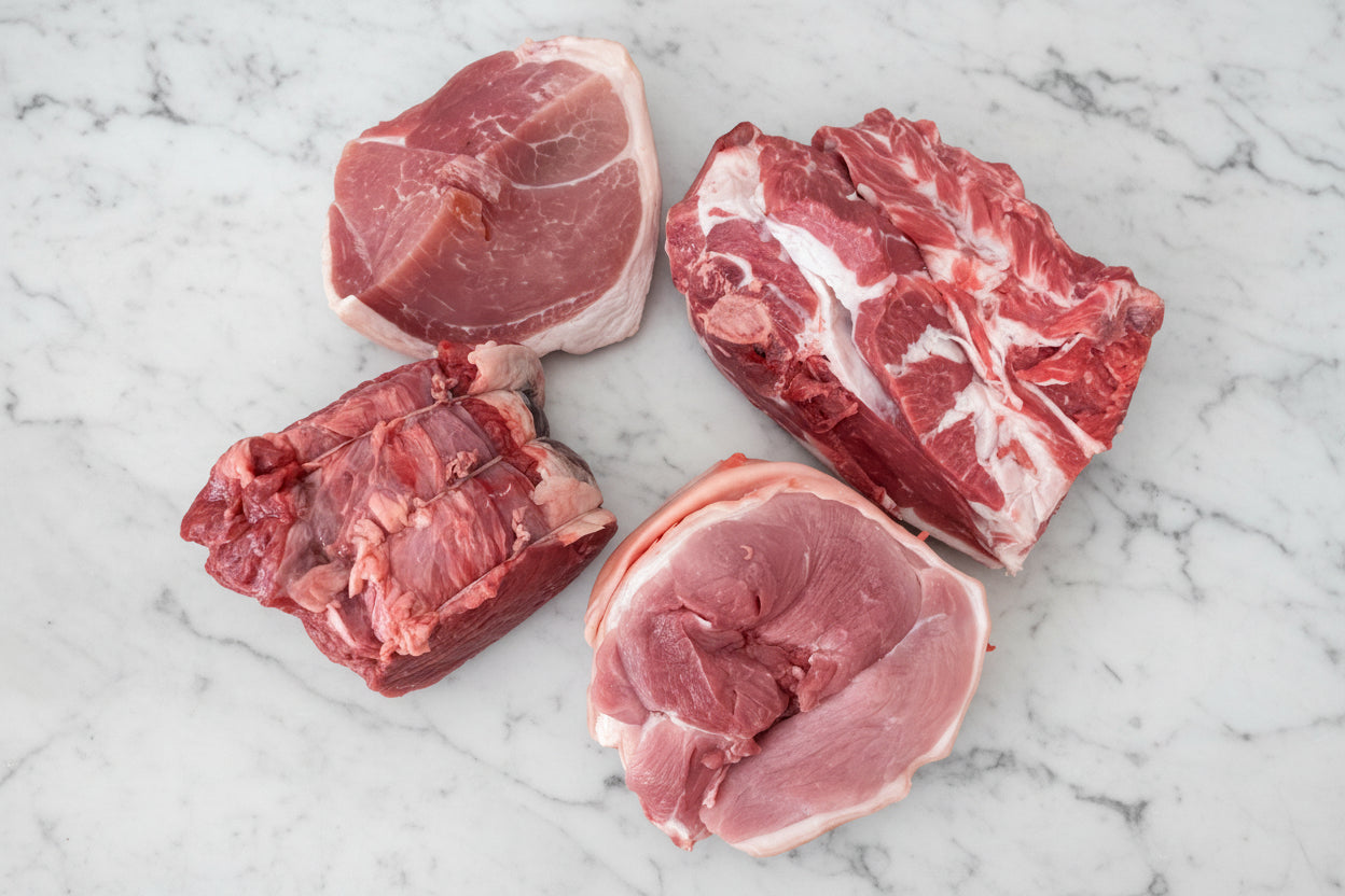 Assorted raw meat joints, including lamb shoulder, silverside beef joint, leg of pork, and gammon joint.
