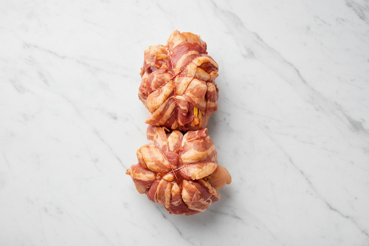 A single chicken breast fillet wrapped in streaky bacon and brushed with BBQ glaze, on a wooden cutting board.